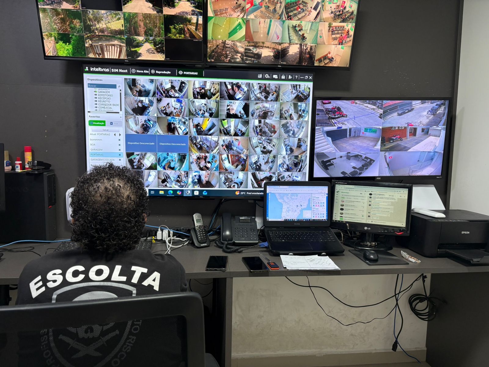 Operador de segurança monitorando diversas câmeras em tempo real em central de controle com múltiplos monitores