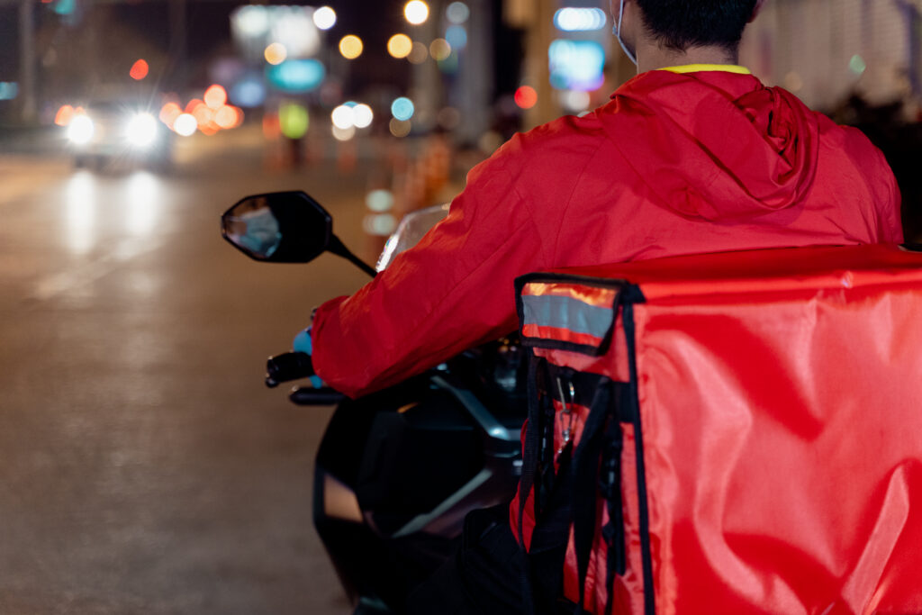 Motociclista com mochila de entrega circulando à noite, tema relacionado à segurança em condomínios residenciais.